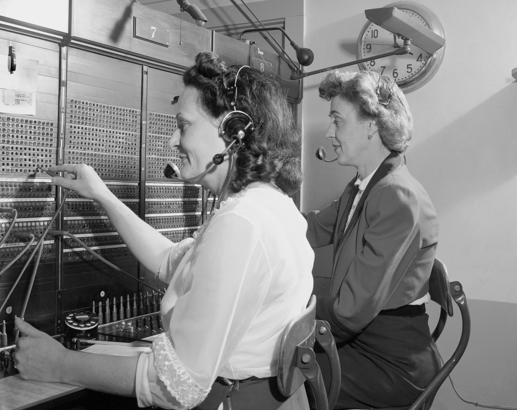 Dos telefonistas con auriculares conectan llamadas en un tablero
